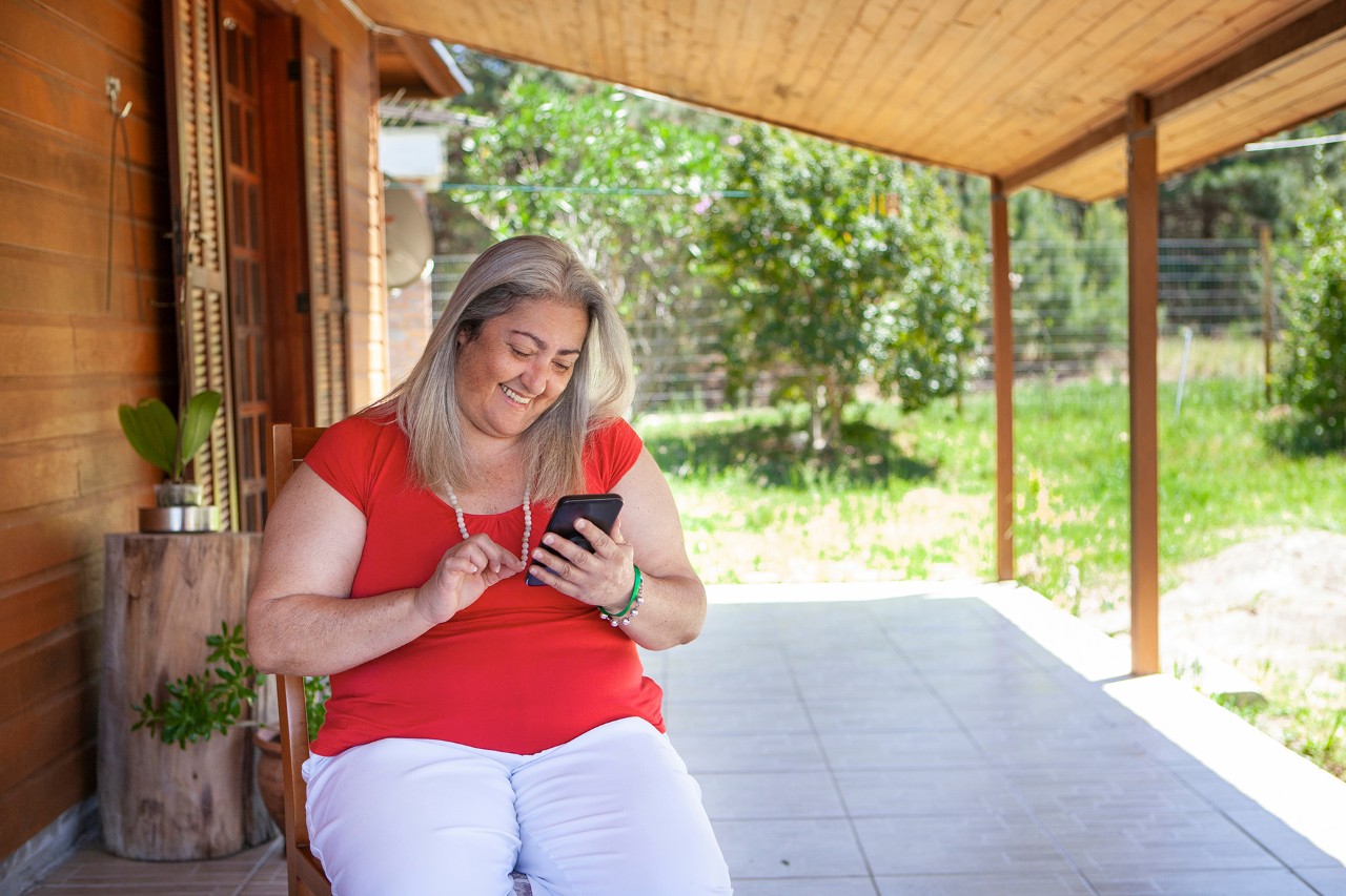 Happy senior woman using smartphone in her front yard in a sunny day