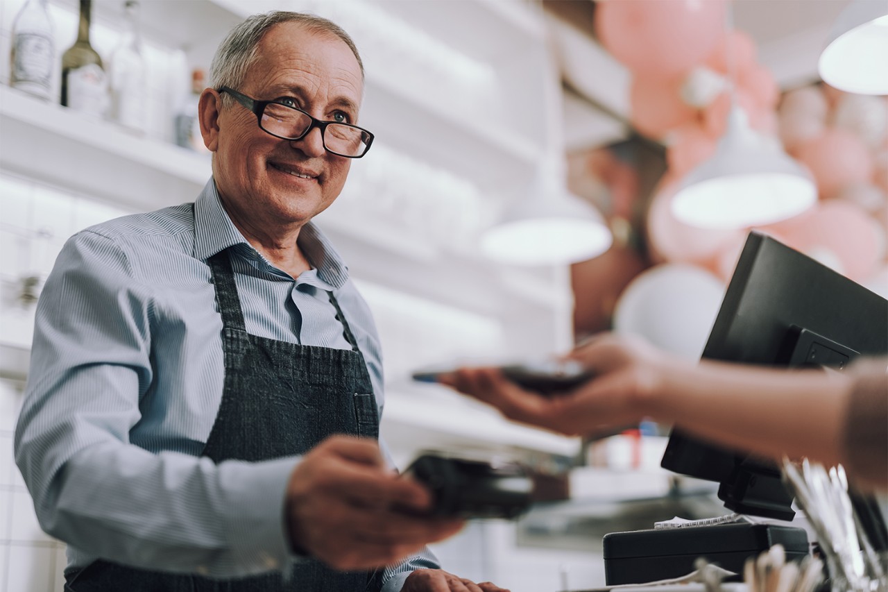 Friendly shop owner in glasses accepting payment from customer
